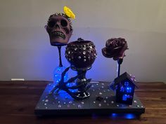 three decorative objects are sitting on a table with blue lights around them and one has a skull, the other is a house