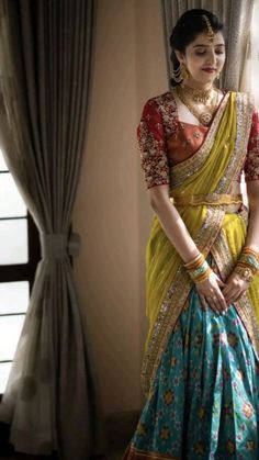 a woman in a yellow and blue sari is standing by a window with her hands on her hips