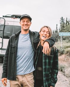 a man and woman standing next to each other in front of a truck on the road