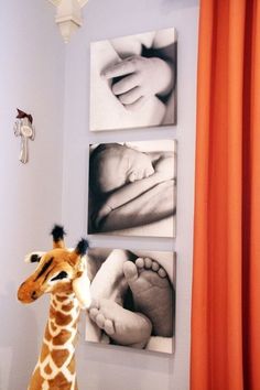 a stuffed giraffe standing in front of three pictures on the wall next to a baby's feet