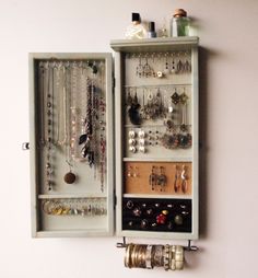 a white wall mounted jewelry cabinet filled with lots of necklaces