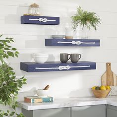 two blue floating shelves on the wall above a counter with bowls, cups and utensils