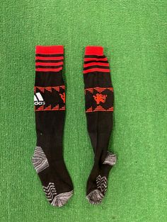 two pairs of socks laying on top of a green carpet with red and black stripes