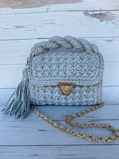 a crocheted purse with a tasselled handle on a white wooden surface