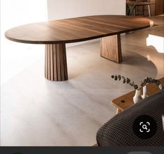 a wooden table sitting on top of a white floor next to a black chair and vase