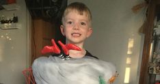 a young boy standing in front of a fake white duck with red feet and legs