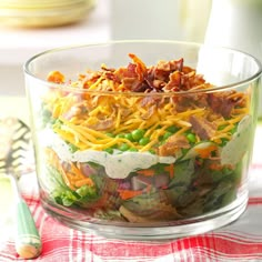 a salad in a glass bowl on a red and white checkered table cloth next to a fork