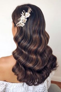 the back of a woman's head with long wavy hair and flowers in her hair