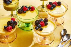 four desserts are arranged in small glasses with berries on top and spoons next to them