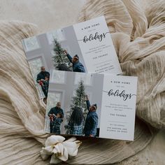 two holiday cards sitting on top of a bed next to a white flower and blanket