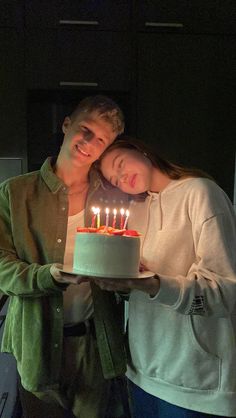 a man and woman holding a cake with lit candles