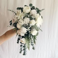 a bridal bouquet being held by someone's hand on a white sheet background