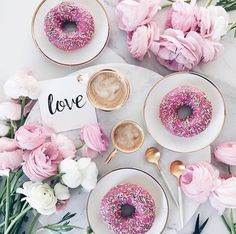 a table topped with donuts covered in pink sprinkles and surrounded by flowers