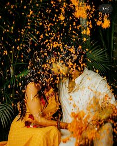 a man and woman sitting next to each other in front of some yellow flowers on the ground