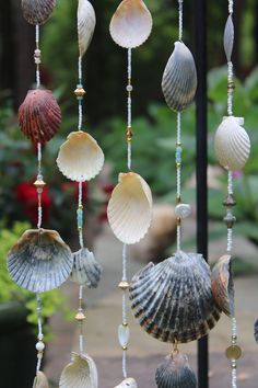 several seashells hanging from a metal rod in front of some plants and bushes