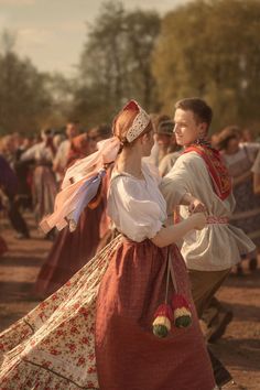 two people dressed in period clothing dancing together at an outdoor event with other people standing around