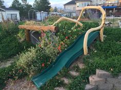 a green slide in the middle of a garden with flowers growing on it's sides