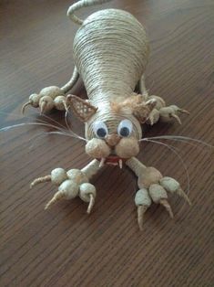 an animal made out of yarn sitting on top of a wooden table with eyes and hands