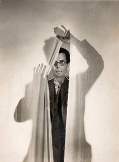 an old black and white photo of a man peeking out from behind a curtain with his hands in the air