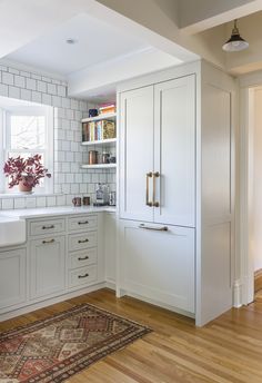 a kitchen with white cabinets and wood flooring next to a rug on the floor