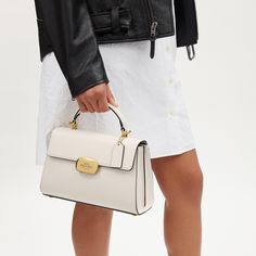 Our Eliza Top Handle has a beloved and timeless silhouette. Crafted of smooth and refined calf leather this bag features multiple inside pockets with plenty of room for essentials like your wallet phone and small accessories. It has a snap closure and an outside open pocket keeping your essentials both secure and easy to access. The detachable strap offers versatile styling options—wear it as a top handle bag or crossbody ideal for both casual and work settings. Elegant Everyday Satchel With Branded Hardware, Elegant Satchel With Branded Hardware For Everyday, Classic Satchel Box Bag With Branded Hardware, Classic Top Handle Box Bag With Branded Hardware, High-end Beige Box Bag, Elegant Satchel With Branded Hardware, Modern Top Handle Box Bag With Branded Hardware, Modern Handheld Satchel With Branded Hardware, Chic Top Handle Satchel With Branded Hardware