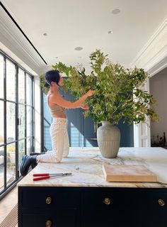 a woman standing on top of a counter next to a vase filled with flowers and greenery