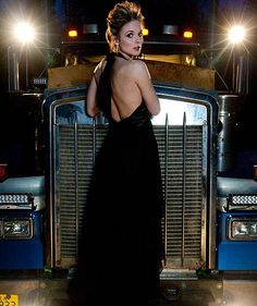 a woman in a black dress standing next to a blue truck with lights on it