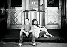 black and white photograph of two people sitting on a bench in front of a building