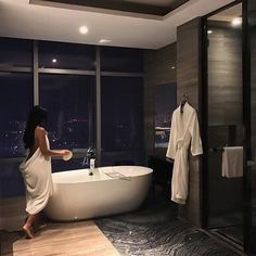 a woman standing in front of a bathtub next to a window with city lights