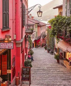 an alley way with people sitting and walking on the sidewalk in front of red buildings