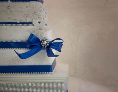 three tiered wedding cake decorated with blue ribbon and beaded decorations on the side