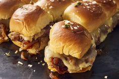 several sliders with meat and cheese on them sitting on a black plate, ready to be eaten