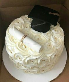 a graduation cake in a box with a black cap and diploma on top, decorated with white icing