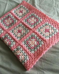 a crocheted pink and gray square on a white bed with a light green comforter