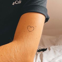 a man's arm with a small heart tattoo on the left side of his arm