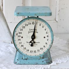 an old blue clock sitting on top of a white table cloth next to a window