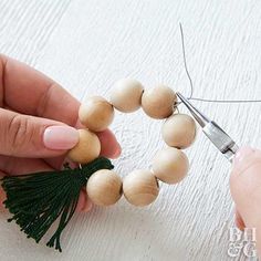 someone is making a bead bracelet with wood beads and green tassels on it