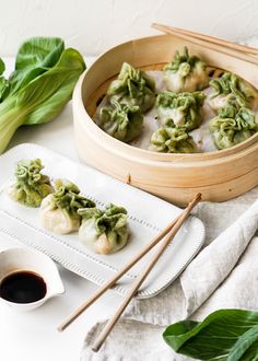 some dumplings are sitting on a plate with chopsticks next to them and green leaves