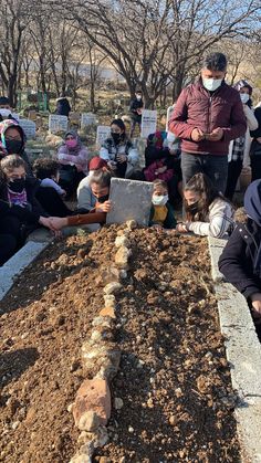 several people are gathered around a pile of dirt and plants, with one person wearing a face mask