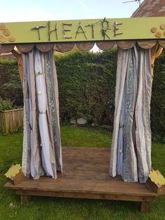 an outdoor stage with curtains and the words theatre written on it in front of some bushes