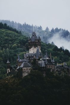 an old castle on top of a hill with fog in the air and trees behind it