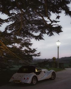 a white car parked on the side of a road next to a lamp post and tree