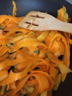 a skillet filled with pasta and cheese being stirred by a wooden utensil