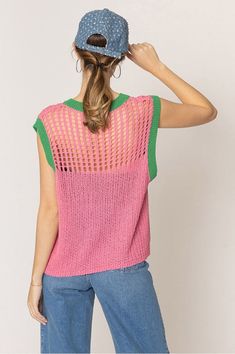 a woman wearing a pink and green knitted top with holes on the back, standing in front of a white wall