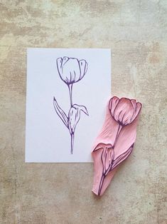 two pink flowers are next to a piece of paper with a drawing of a flower on it