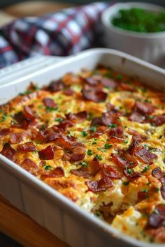 a casserole dish with bacon and cheese in it on a wooden table next to two bowls