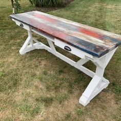 an old wooden table is painted white and blue with red paint on the top, sitting in grass