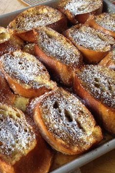 powdered sugar covered pastries in a pan on top of a wooden countertop