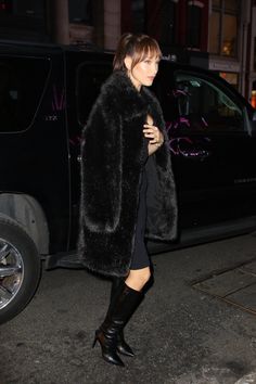 a woman in black boots and a fur coat is walking down the street at night