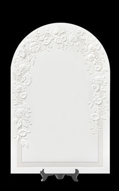 a white plate with an ornate design on the front and sides, against a black background